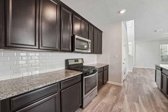 Kitchen featuring appliances with stainless steel finishes, light wood-style flooring, light stone counters, decorative backsplash, and a textured ceiling | Image 5