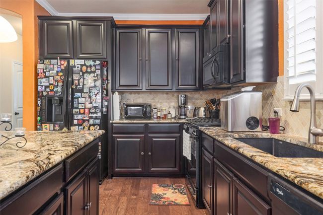 Kitchen with black appliances, a sink, dark wood-type flooring, crown molding, and backsplash | Image 5