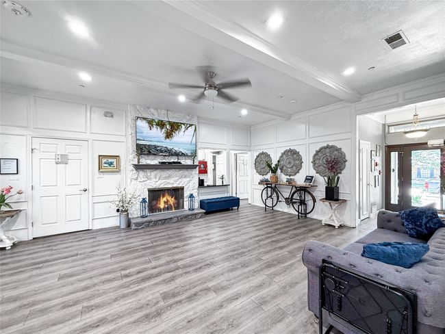 Living room with a decorative wall, beam ceiling, ceiling fan, a stone fireplace, and light wood-style flooring | Image 9