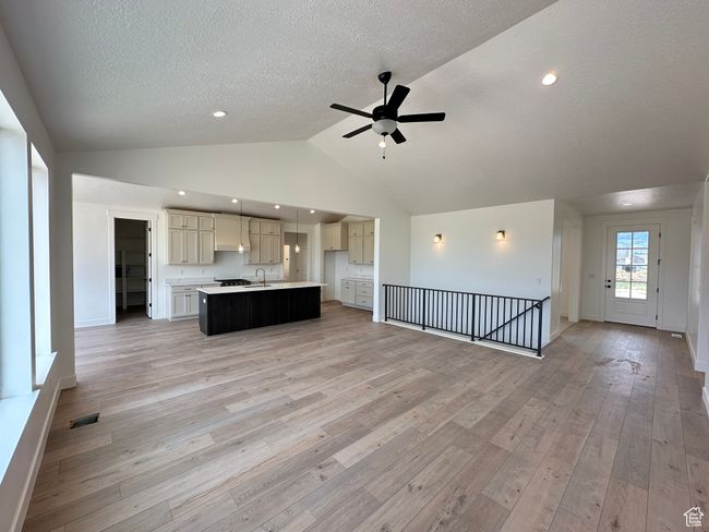 Unfurnished living room featuring a textured ceiling, a ceiling fan, vaulted ceiling, and light wood finished floors | Image 6