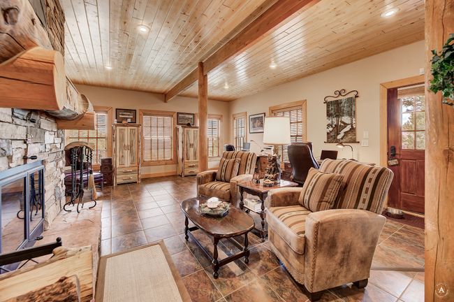 Living room with a fireplace, a wood ceiling with exposed beams, recessed lighting, and tile patterned floors | Image 51