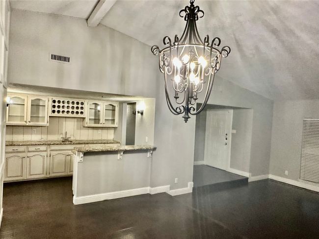 Kitchen with beamed ceiling, glass insert cabinets, a chandelier, light stone counters, and cream cabinets | Image 7