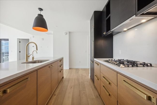 Kitchen with light wood-style flooring, light countertops, hanging light fixtures, stainless steel gas cooktop, and premium range hood | Image 8