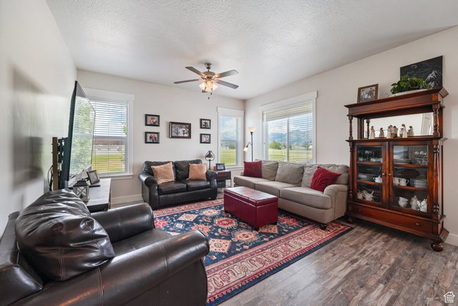 Living area with healthy amount of natural light, a ceiling fan, dark wood-type flooring, and a textured ceiling | Image 11