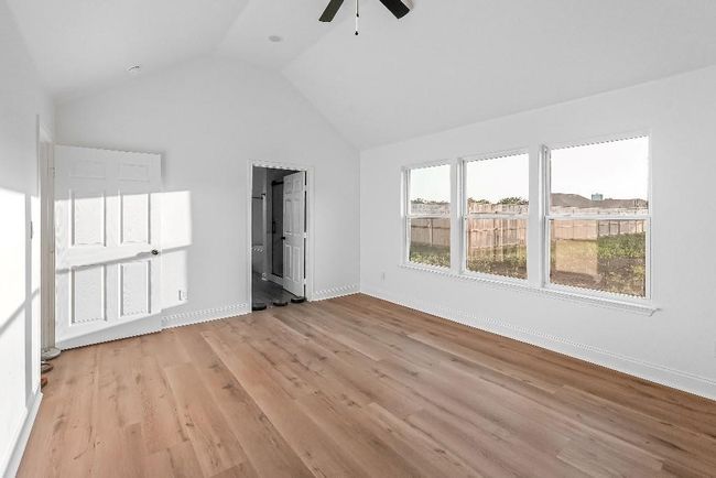 Unfurnished bedroom with ceiling fan, baseboards, ensuite bathroom, lofted ceiling, and light wood-type flooring | Image 15