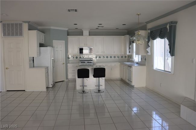 Kitchen featuring white appliances, a kitchen breakfast bar, tasteful backsplash, light tile patterned flooring, and ornamental molding | Image 30