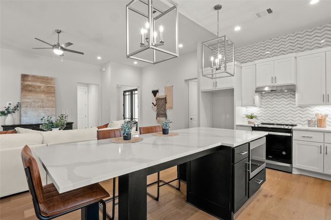 Kitchen with open floor plan, range with electric stovetop, dark cabinetry, under cabinet range hood, and visible vents | Image 12