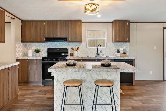 Kitchen with a sink, a kitchen bar, wood finished floors, under cabinet range hood, and black appliances | Image 16