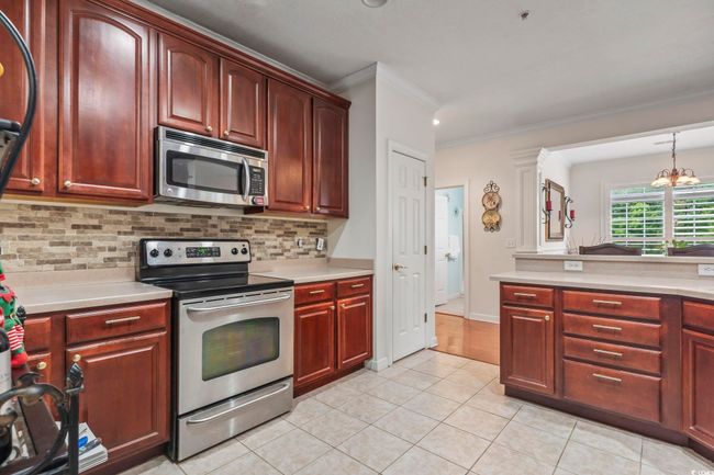 Kitchen featuring stainless steel appliances, crown molding, reddish brown cabinets, light countertops, and backsplash | Image 19