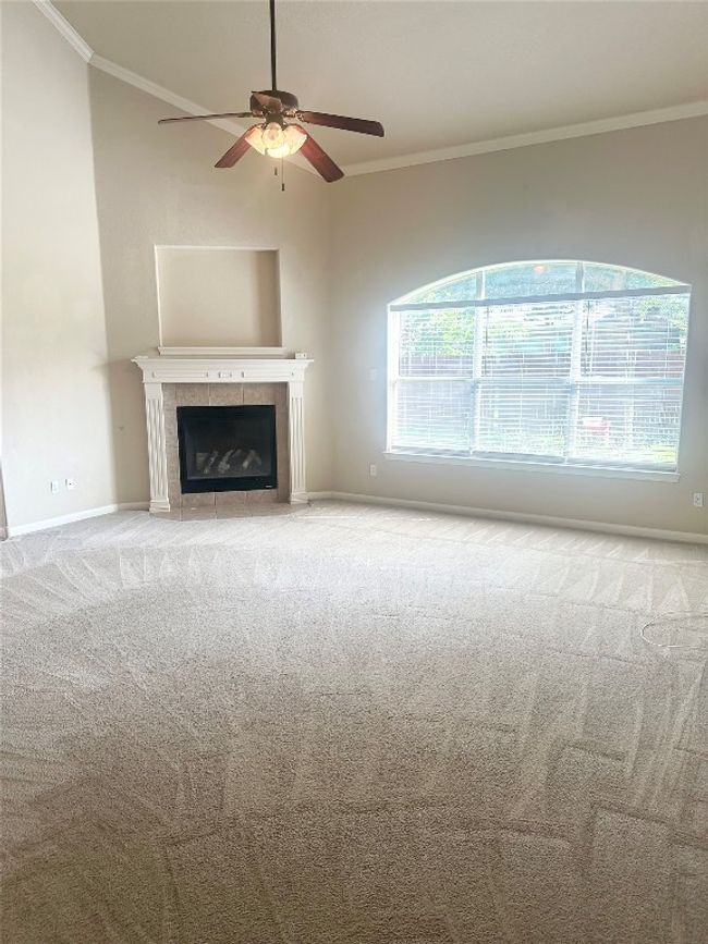 Unfurnished living room featuring ornamental molding, a ceiling fan, carpet flooring, and a tiled fireplace | Image 5