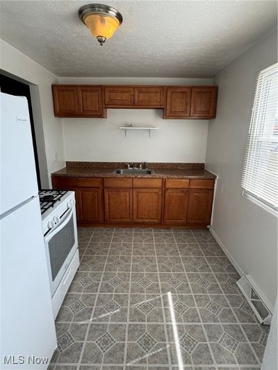 Kitchen with stove, refrigerator, a textured ceiling, and sink | Image 3