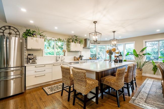 Kitchen featuring stainless steel appliances, wall chimney range hood, white cabinets, light countertops, and recessed lighting | Image 7