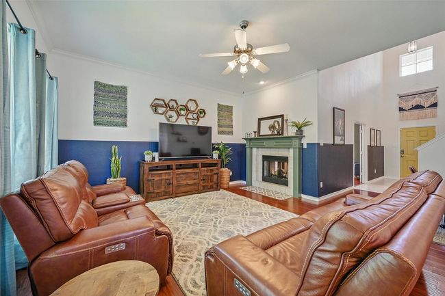 Living area with wood finished floors, ceiling fan, crown molding, a fireplace, and baseboards | Image 7