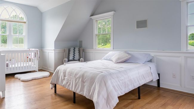 Bedroom featuring lofted ceiling, a decorative wall, wood finished floors, and wainscoting | Image 17