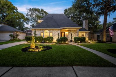 Charming 2-story home with well-manicured landscaping, featuring a welcoming entrance, external lighting, and a detached two-car garage. The home's traditional architecture is complemented by a neat, circular garden bed and a prominently displayed American flag. | Image 1