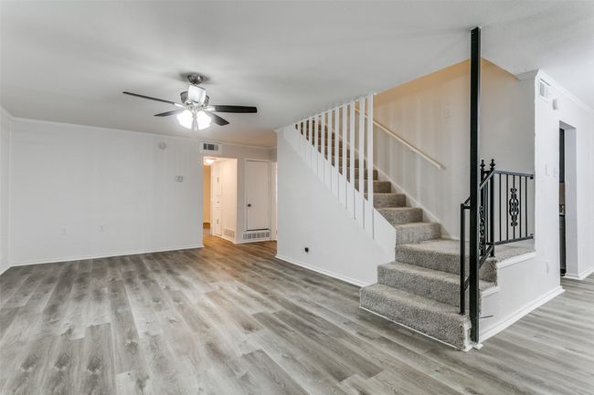 Unfurnished living room with stairway, a ceiling fan, wood finished floors, baseboards, and visible vents | Image 6