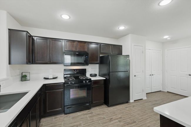 Kitchen featuring light wood-style flooring, a sink, dark brown cabinets, light countertops, and black appliances | Image 4