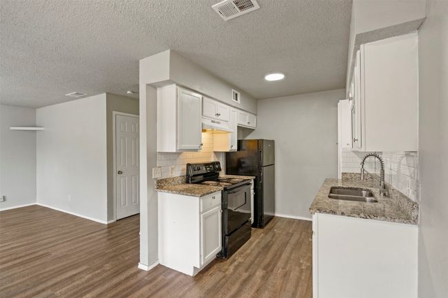 Kitchen with black appliances, a sink, dark wood finished floors, tasteful backsplash, and a textured ceiling | Image 10