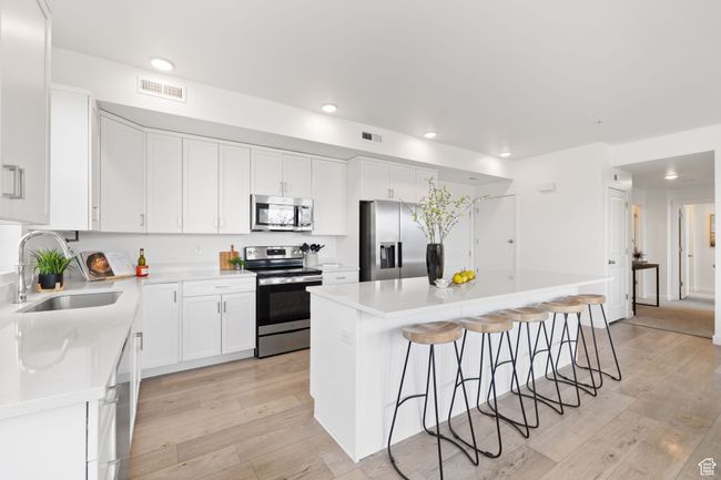 Kitchen featuring stainless steel appliances, a kitchen bar, a center island, light wood finished floors, and white cabinetry | Image 13