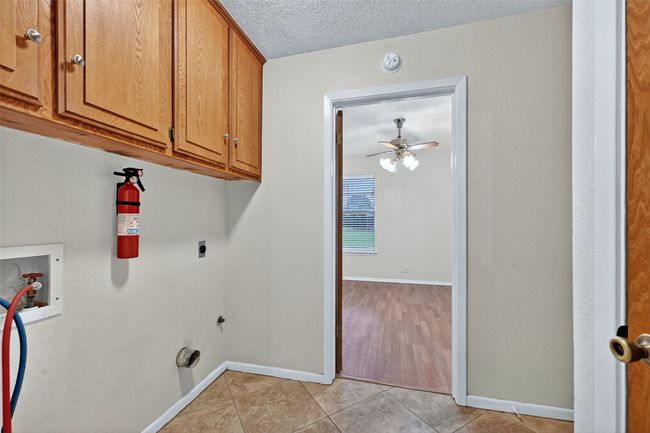 Washroom with washer hookup, cabinet space, hookup for an electric dryer, light tile patterned floors, and a textured ceiling | Image 10