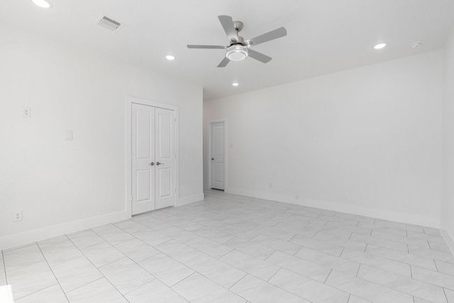 This spacious room features clean white walls and tile flooring, complemented by a ceiling fan and recessed lighting. A double-door closet and additional doorway provide ample storage and access. | Image 28