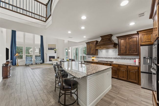 Kitchen with premium range hood, a sink, light stone counters, a warm lit fireplace, and healthy amount of natural light | Image 13