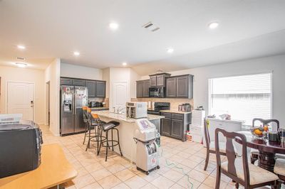 Kitchen with stove, decorative backsplash, a kitchen island with sink, stainless steel fridge with ice dispenser, and a kitchen breakfast bar | Image 2