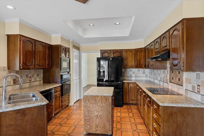 Kitchen featuring light tile patterned flooring, black appliances, decorative backsplash, sink, and a center island | Image 6