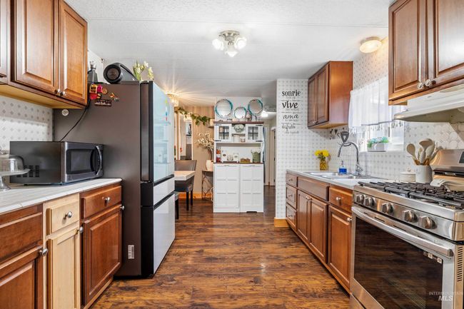 Kitchen with stainless steel appliances, dark wood-style floors, light countertops, under cabinet range hood, and backsplash | Image 7