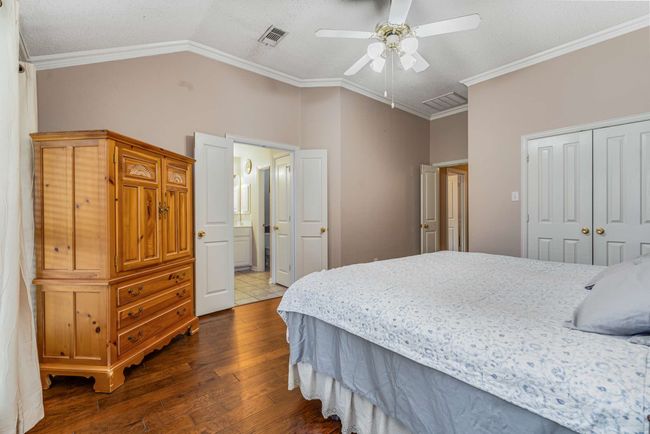 Bedroom featuring hardwood finished floors, a walk-in closet, vaulted ceiling, ornamental molding, and ceiling fan | Image 24