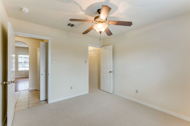Unfurnished bedroom with light colored carpet, ceiling fan, light tile patterned floors, a walk in closet, and arched walkways | Image 18