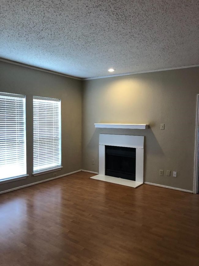 Unfurnished living room with a fireplace with raised hearth, a textured ceiling, crown molding, recessed lighting, and wood finished floors | Image 5