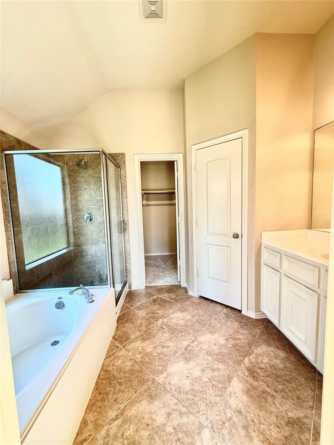This bathroom features a spacious layout with a tiled floor, a glass-enclosed shower, a large soaking tub, and dual sinks with a vanity. It includes a walk-in closet and neutral-toned walls for a bright and inviting atmosphere. | Image 15