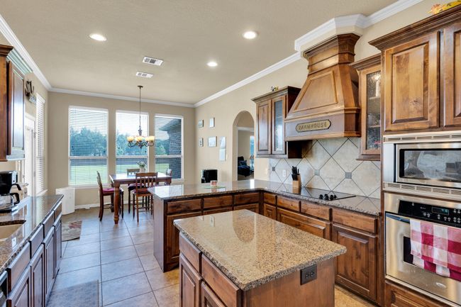 Kitchen featuring stainless steel appliances, a peninsula, brown cabinets, arched walkways, and ornamental molding | Image 8