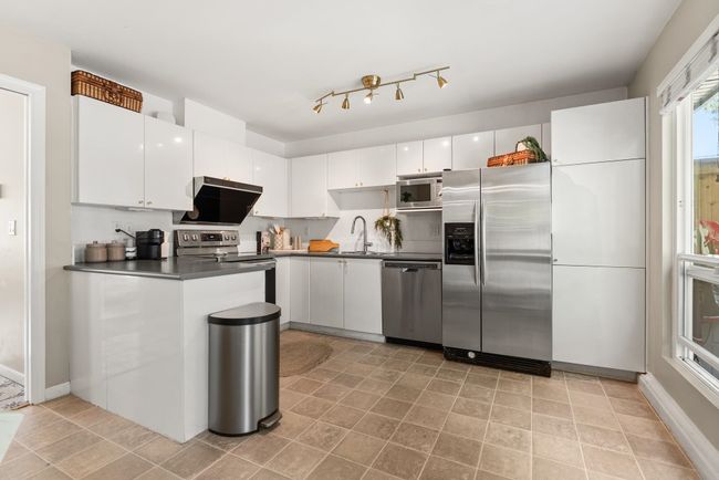 Kitchen featuring stainless steel appliances, a sink, dark countertops, white cabinetry, and baseboards | Image 19
