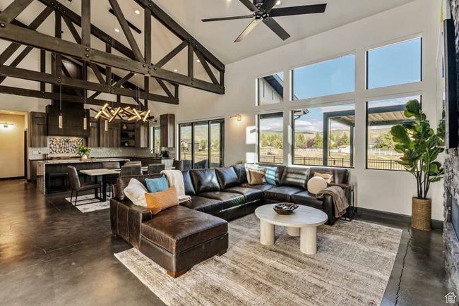 Living room featuring beam ceiling, finished concrete floors, ceiling fan, high vaulted ceiling, and baseboards | Image 12