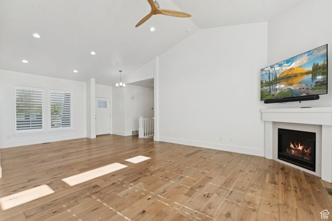 Unfurnished living room with a glass covered fireplace, ceiling fan, recessed lighting, light wood finished floors, and high vaulted ceiling | Image 4