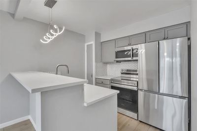 Kitchen featuring light hardwood / wood-style floors, hanging light fixtures, stainless steel appliances, kitchen peninsula, and decorative backsplash | Image 1