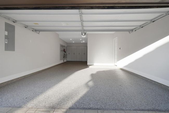 The spacious three-car tandem garage with a clean, finished interior. It features a polished concrete floor, built-in storage cabinets, and wall-mounted organization systems, offering ample storage and workspace. The space is well-lit with LED overhead lighting and includes a side access door to the home. | Image 6