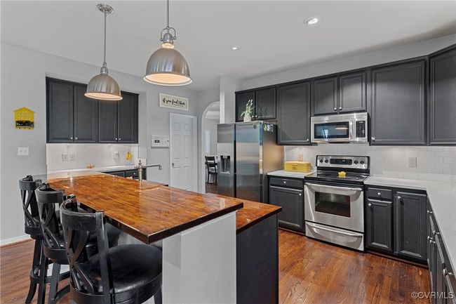 Kitchen featuring tasteful backsplash, hanging light fixtures, butcher block countertops, stainless steel appliances, and dark wood-style flooring | Image 4