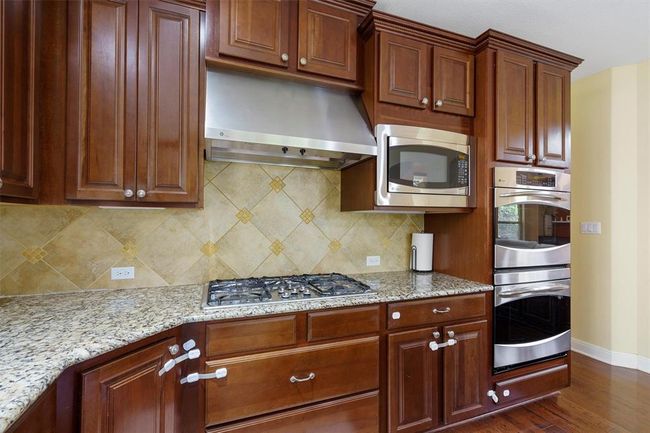 Kitchen with appliances with stainless steel finishes, ventilation hood, baseboards, dark wood finished floors, and light stone counters | Image 13