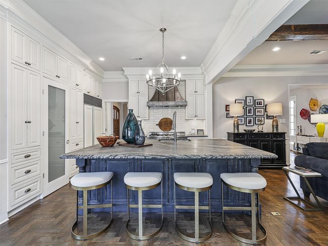 Kitchen featuring a kitchen breakfast bar, a chandelier, tasteful backsplash, white cabinetry, and ornamental molding | Image 13
