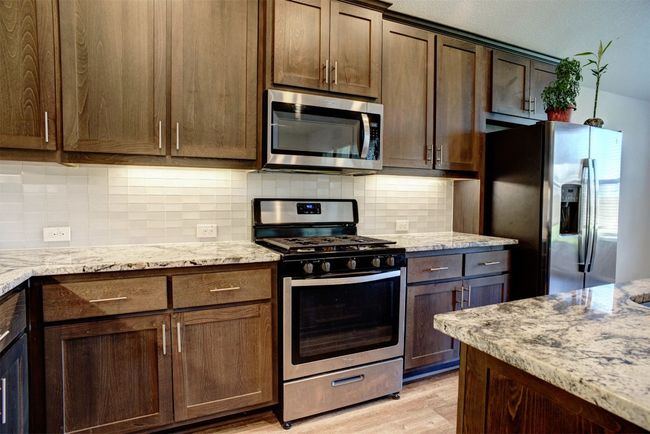 Kitchen with light stone counters, appliances with stainless steel finishes, dark brown cabinets, and light wood-style floors | Image 13