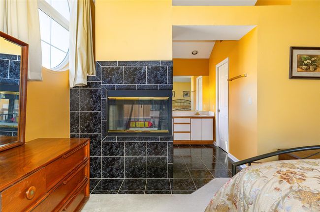 Primary Bedroom featuring a tiled fireplace, tile walls, and vaulted ceiling | Image 26