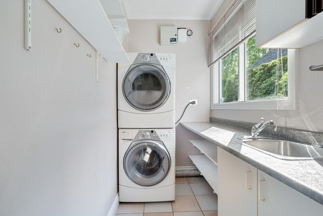 Washroom featuring a sink, stacked washing maching and dryer, light tile patterned flooring, ornamental molding, and cabinet space | Image 29