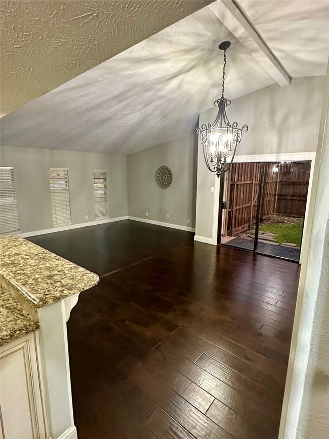Open dining area with wood-type flooring, a textured ceiling, vaulted ceiling, and a chandelier | Image 9