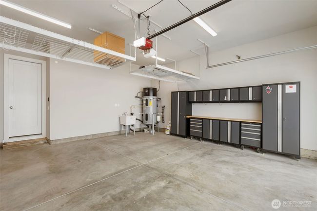 This spacious two-car garage is fully equipped with overhead storage racks, a utility sink, and a custom wall-mounted cabinet system with workbench—perfect for hobbies, tools, and organized storage. It also features an electric car charger, making it ideal for modern living and eco-conscious convenience. | Image 37