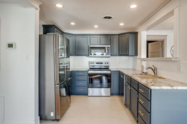 Kitchen featuring appliances with stainless steel finishes, ornamental molding, tasteful backsplash, light stone counters, and a sink | Image 16