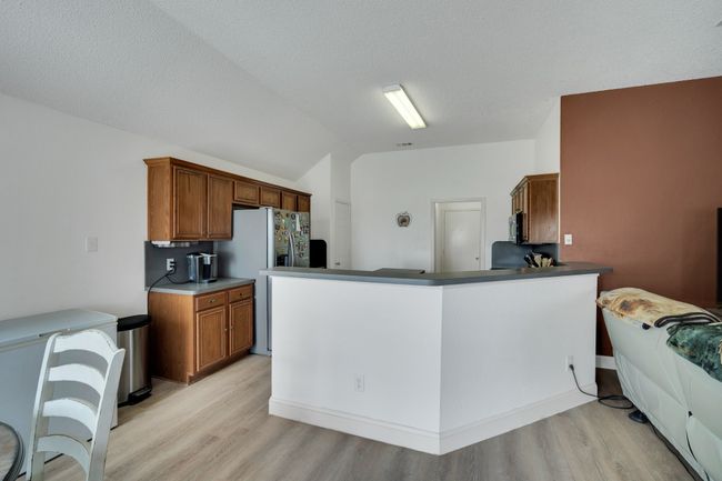 Kitchen with light wood-style flooring, lofted ceiling, refrigerator with ice dispenser, brown cabinetry, and a peninsula | Image 12