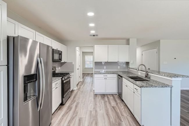 Kitchen featuring appliances with stainless steel finishes, visible vents, a sink, a peninsula, and light wood-type flooring | Image 4